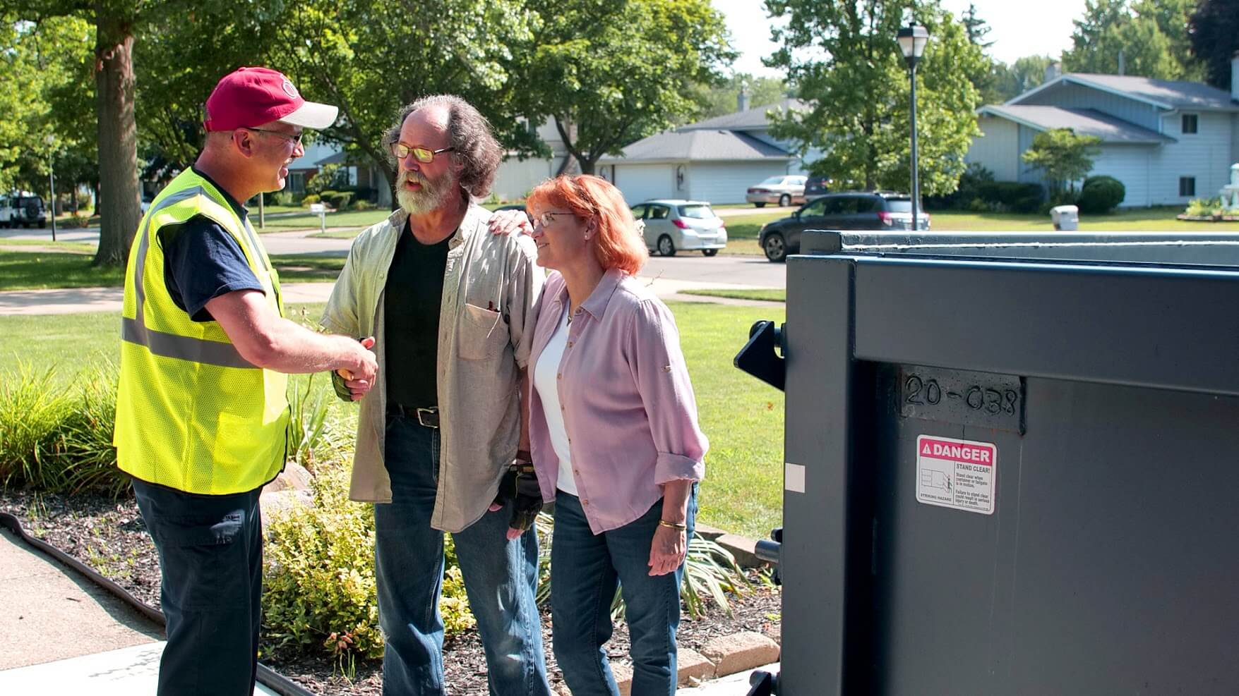 Two homeowners speaking with a dumpster delivery man.