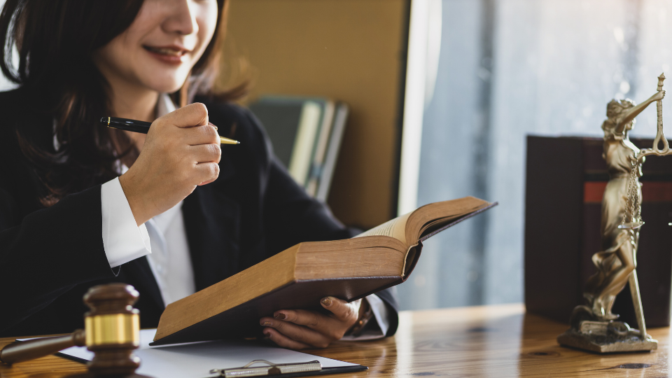A person in a business suit sitting at a desk with an open book and a gavel in front of them