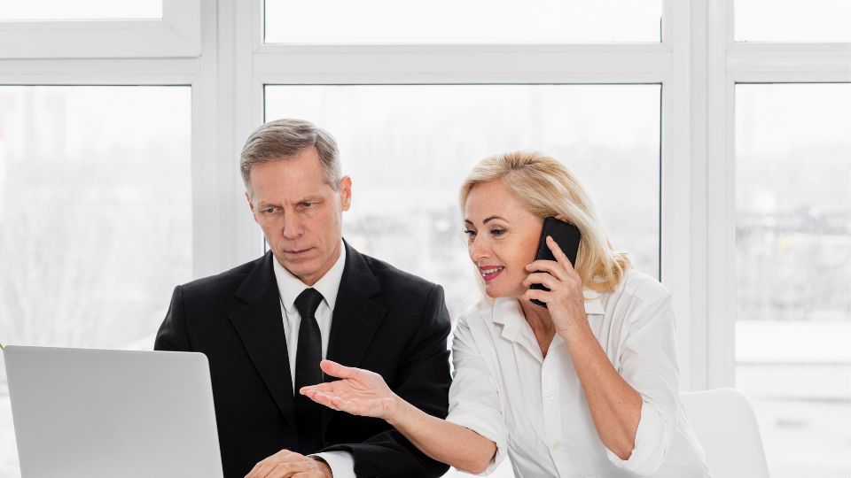 Two professionals looking at a laptop while one speaks on the phone.