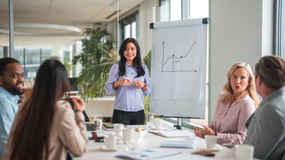 A group of professionals engaged in discussion, with one presenting data displayed on a whiteboard.