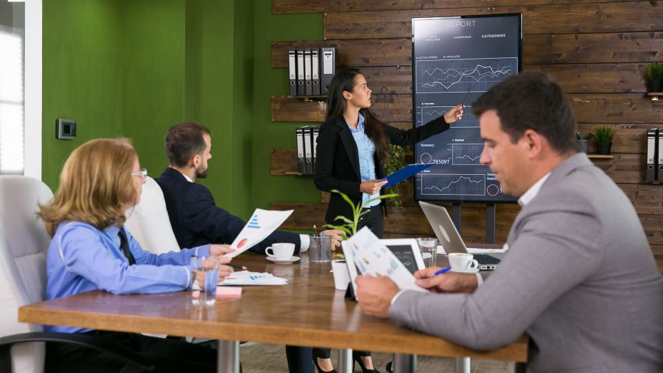An employee leading a business meeting in an office with colleagues seated at a table